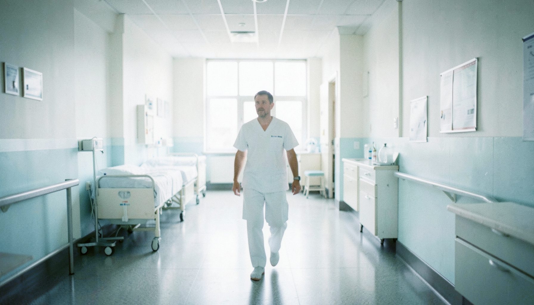Corredor de hospital com luz natural difusa, tons de branco e azul claro, ambiente calmo e acolhedor, sem pessoas visíveis.